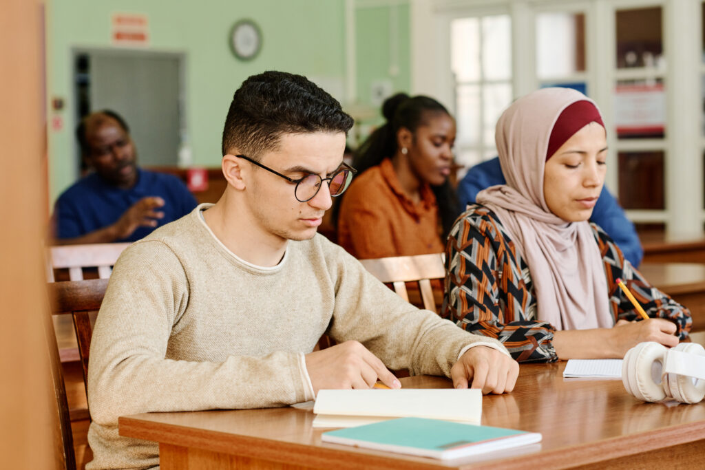 Group of immigrant students in international class sitting at desk reading and making notes during lesson