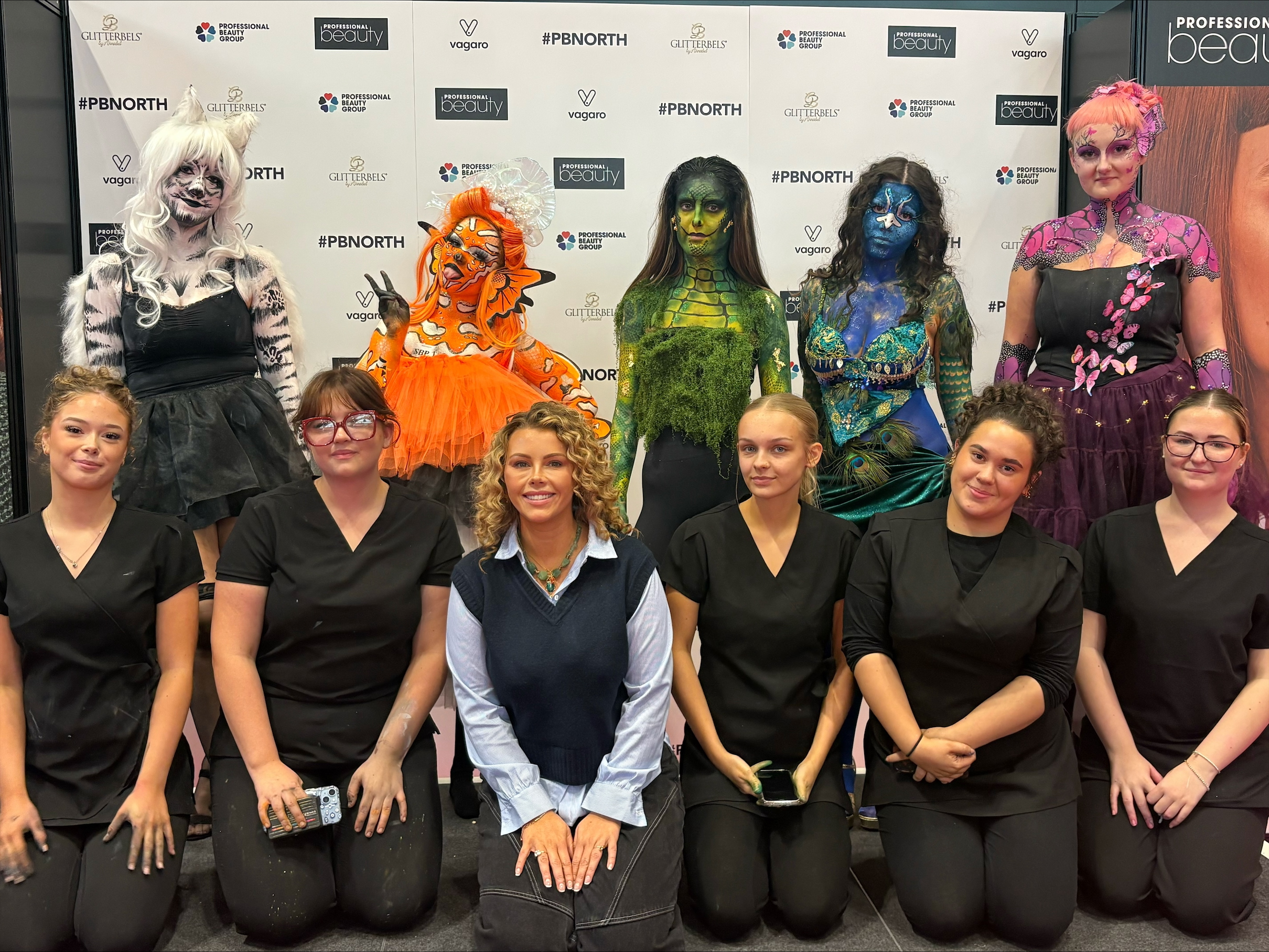 Group photo featuring costumed participants in the back row and event staff in black attire in the front row.