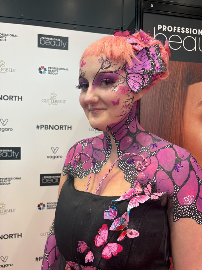 Close-up of a person in pink butterfly-themed body paint with floral designs across arms and chest