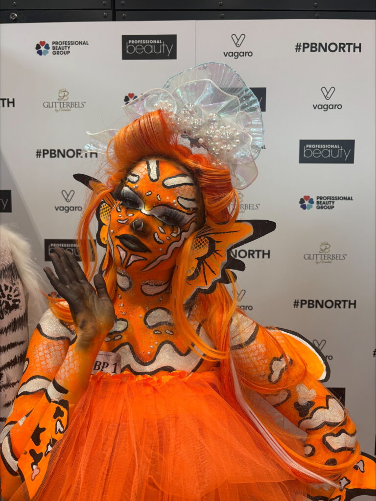 Close-up of a person in orange fish-themed costume with scale-like face paint and tulle dress.